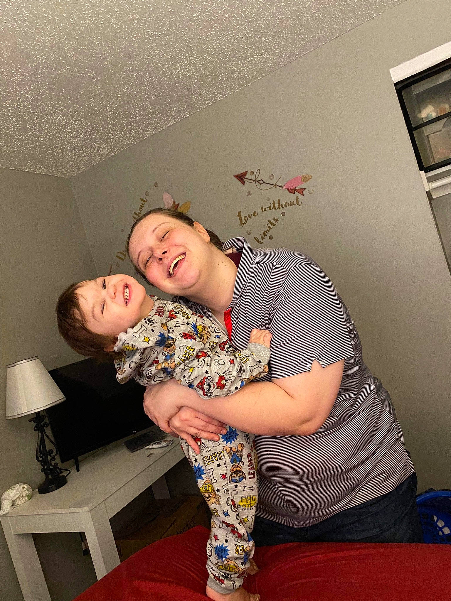 Ezra is registered to the contest to win money with this photo: abdomen, ceiling, comfort, elbow, eyewear, flooring, fun, happy, human_leg, joint, joy, knee, lamp, person, pillow, pink, room, shorts, sitting, smile