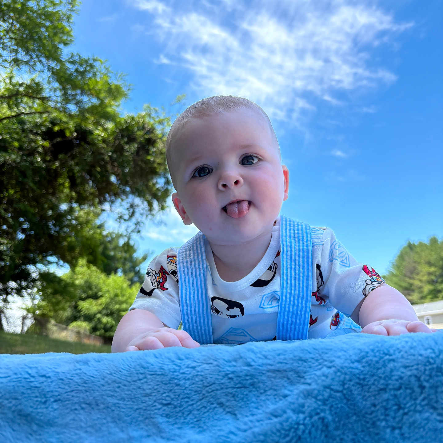 Carter joined the competition — help win amazing prizes! baby, child, tongue_out, blue_blanket, outdoor, sky, clouds, trees, greenery, cute, playful, infant, smiling, daylight, nature, grass, portrait, toddler, casual_clothing, happy