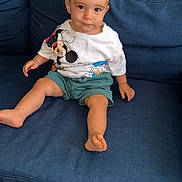 Ayden a rejoint le concours — aidez-le/la à gagner de superbes lots ! toddler, child, blue_couch, mickey_mouse, donald_duck, tshirt, shorts, barefoot, smiling, sitting, indoors, tile_floor, hair, face, person, young_child, casual_clothing, furniture, home, cute