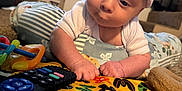 Rogan is registered to the contest to win money with this photo: baby, infant, hat, toy, controller, remote_control, play_mat, indoor, carpet, curious, crawling, child, colorful, striped_hat, soft_toys, window, pillow, cushion, hands, face