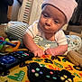baby, infant, hat, toy, controller, remote_control, play_mat, indoor, carpet, curious, crawling, child, colorful, striped_hat, soft_toys, window, pillow, cushion, hands, face