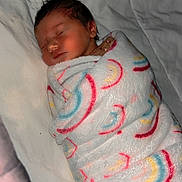 Rayann is registered to the contest to win money with this photo: baby, newborn, sleeping, blanket, rainbow_pattern, infant, wrapped, soft_texture, cozy, resting, cute, child, bed, sleep, peaceful, indoors, portrait, human, warm, comfort