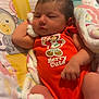 baby, sleeping, blanket, onesie, orange_clothing, cartoon_character, patterned_baby_seat, monkey, giraffe, soft_texture, infant, cute, peaceful, child, foot, hand, face, indoor, colorful, cozy