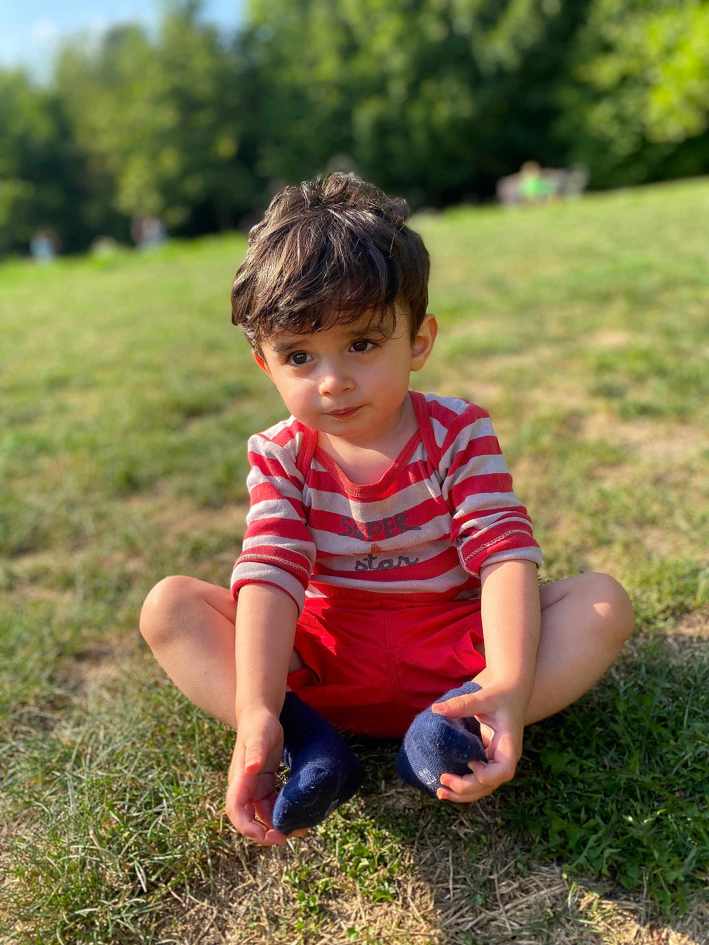 élio participe au concours pour gagner de l'argent avec cette photo : child, boy, grass, outdoor, sitting, red_shorts, striped_shirt, socks, cute, sunlight, nature, portrait, young, casual_clothing, daylight, playful, greenery, expression, knees_up, summer