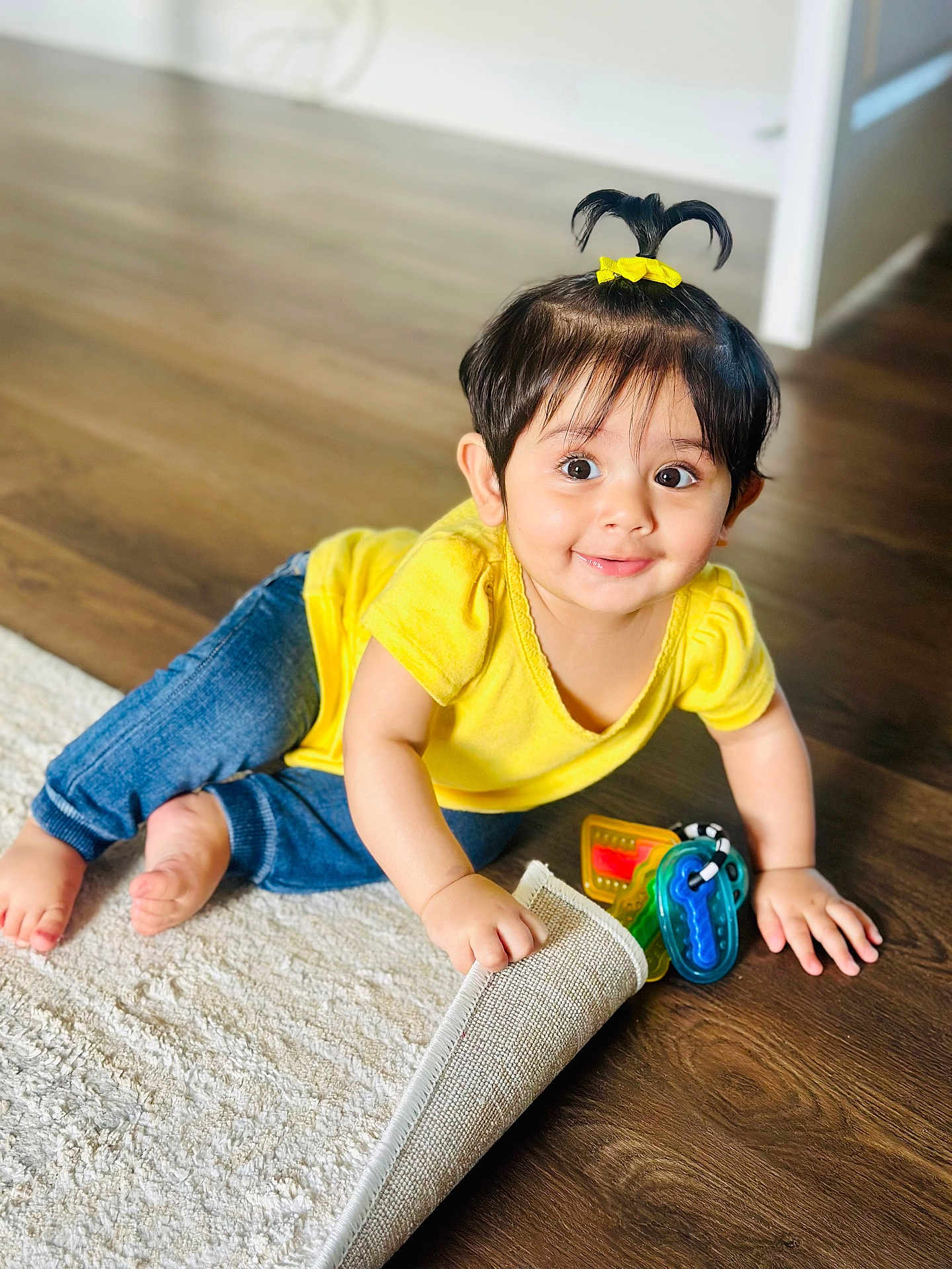 Guleen joined the competition — help win amazing prizes! toddler, child, yellow_shirt, blue_jeans, toy_keys, wooden_floor, white_rug, hair_tie, pony_tail, smiling, indoors, cute, playful, happy, baby, crawling, curious, bright_eyes, small_hands, floor