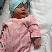 Paloma participe au concours pour gagner de l'argent avec cette photo : baby, sleeping, pink_onesie, head_wrap, bow, bed, white_sheet, infant, soft_fabric, peaceful, cute, child, newborn, human, resting, hand, footwear, indoors, portrait, cozy