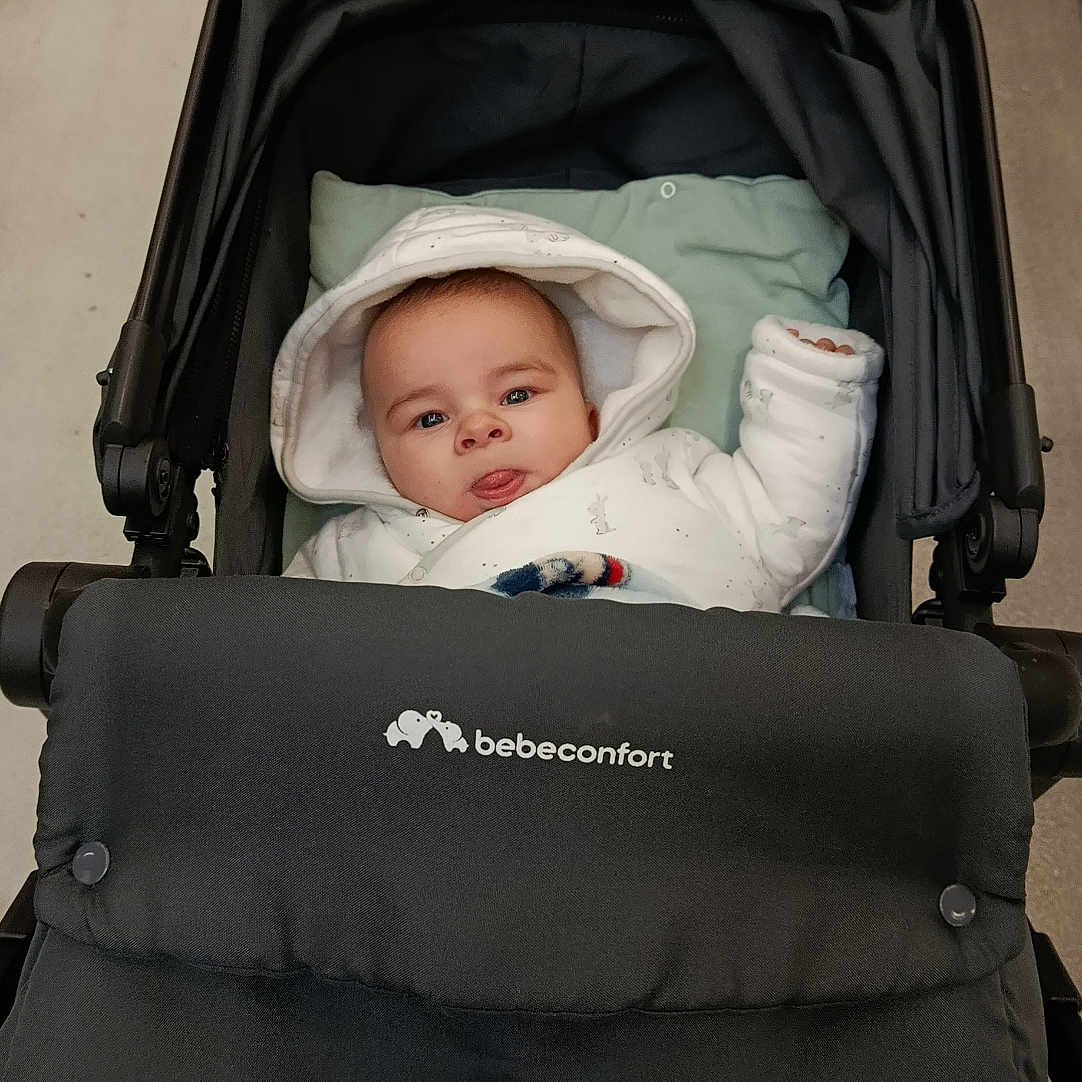 Zayon a rejoint le concours — aidez-le/la à gagner de superbes lots ! baby, bebeconfort, blanket, clothing, cozy, cute, eyes, face, floor, handle, hood, indoor, infant, onesie, padded_seat, portrait, pram, sitting, stroller, tongue