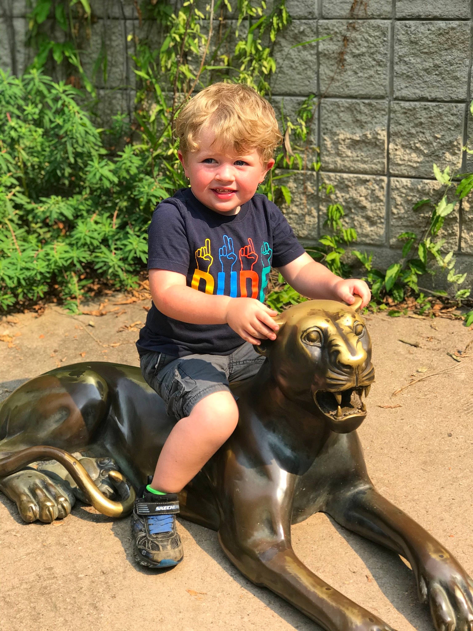 Carter is registered to the contest to win money with this photo: art, fawn, fun, grass, happy, lawn_ornament, leg, leisure, mammal, person, plant, recreation, reptile, sculpture, shorts, smile, statue, terrestrial_animal, toddler, vertebrate