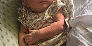 Kora is registered to the contest to win money with this photo: arms, baby, blanket, cozy, cute, expression, face, floral_onesie, hand, indoor, infant, legs, natural_light, newborn, person, pillow, resting, serious, skin, soft_texture