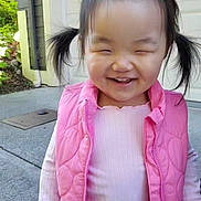 Abbie is registered to the contest to win money with this photo: child, girl, pigtails, pink_vest, smiling, outdoor, daylight, happy, cute, hair_clip, face, person, long_sleeve_shirt, concrete, background, building, expression, young, casual_clothing, portrait