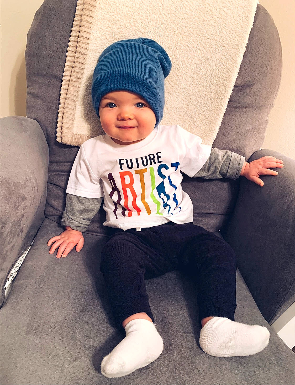 Lawson is registered to the contest to win money with this photo: ankle, armrest, baby, baby_toddler_clothing, barefoot, beanie, bonnet, child, comfort, couch, foot, headwear, knit_cap, lap, living_room, person, sitting, slipcover, sock, toddler