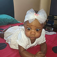 Alaina is registered to the contest to win money with this photo: baby, infant, child, white_dress, headband, bow, wide_eyes, bed, polka_dots, red_bedspread, indoor, cute, expression, tummy, skin, person, furniture, pillow, black, photography