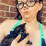 woman, kitten, cat, holding, hand, tattoo, glasses, filter, bear_ears, brick_wall, tank_top, blue_clothing, portrait, outdoor, pet, cute, animal, young, casual, close_up
