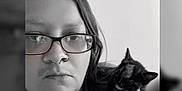 Nebula Star is registered to the contest to win money with this photo: person, glasses, cat, tortoiseshell_cat, black_and_white, portrait, indoor, hand, face, hair, serious, close_up, shoulder, nose_ring, jewelry, watching, pet, animal, companion, calm
