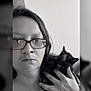 person, glasses, cat, tortoiseshell_cat, black_and_white, portrait, indoor, hand, face, hair, serious, close_up, shoulder, nose_ring, jewelry, watching, pet, animal, companion, calm