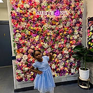 Alanna joined the competition — help win amazing prizes! child, girl, blue_dress, flower_wall, neon_sign, lollipop, pose, plant, potted_plant, indoor, floor, bulletin_board, notes, attitude, colorful, decor, fashion, portrait, standing, playful
