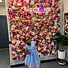 child, girl, blue_dress, flower_wall, neon_sign, lollipop, pose, plant, potted_plant, indoor, floor, bulletin_board, notes, attitude, colorful, decor, fashion, portrait, standing, playful