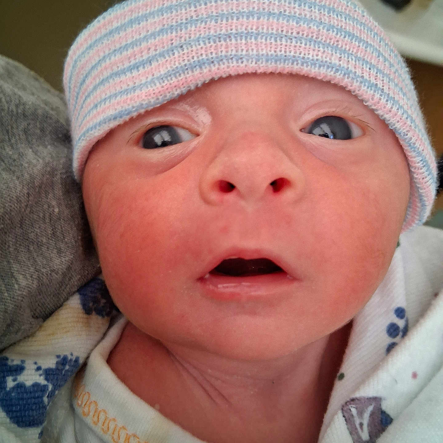 Carson is registered to the contest to win money with this photo: baby, blanket, child, close_up, clothing, cute, expression, eyes, face, hat, headwear, indoors, infant, mouth, newborn, person, portrait, skin, striped_hat, young