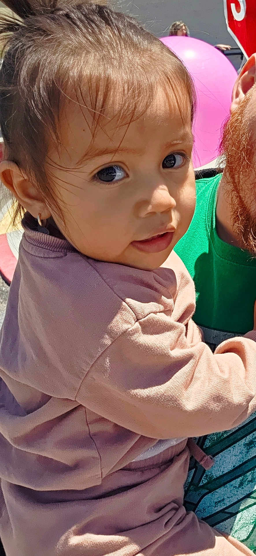 Luciana joined the competition — help win amazing prizes! toddler, child, person, face, clothing, pink_outfit, green_shirt, balloon, stop_sign, outdoor, daylight, hair, earring, bench, beard, curious_expression, close_up, holding, urban, sunlight