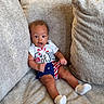 Ashton joined the competition — help win amazing prizes! baby, couch, cushion, infant, clothing, white_socks, 4th_of_july, surprised, seated, indoors, plush, beige, cute, child, person, portrait, comfortable, fabric, home, expression
