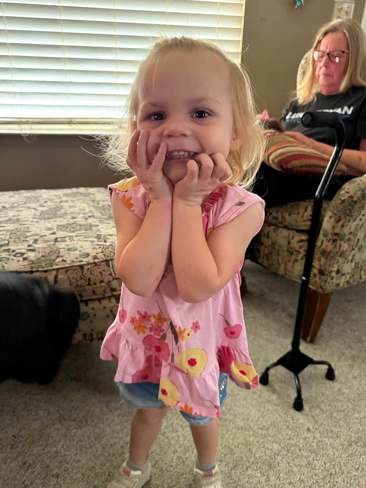 Peyton is registered to the contest to win money with this photo: child, girl, smile, happy, indoor, living_room, woman, phone, armchair, dog, carpet, window_blinds, patterned_furniture, casual_clothing, footwear, blonde_hair, person, home, cute, playful
