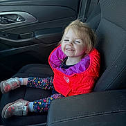 Peyton is registered to the contest to win money with this photo: child, toddler, smiling, car, car_interior, jacket, red_jacket, purple_lining, leggings, floral_pattern, shoes, silver_shoes, seat, seatbelt, window, door, happy, person, cute, young_child