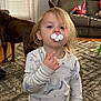 toddler, child, indoor, pajamas, unicorn_pattern, pacifier, bunny_shape, dog, brown_dog, carpet, couch, window_blinds, toy_basket, living_room, person, curly_hair, floor, wood_floor, furniture, cute