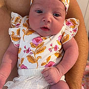 Amara is registered to the contest to win money with this photo: baby, infant, child, floral_clothing, headband, arm, hand, skin, cute, newborn, person, portrait, holding, pink, white, pattern, flower, expression, indoors, closeup