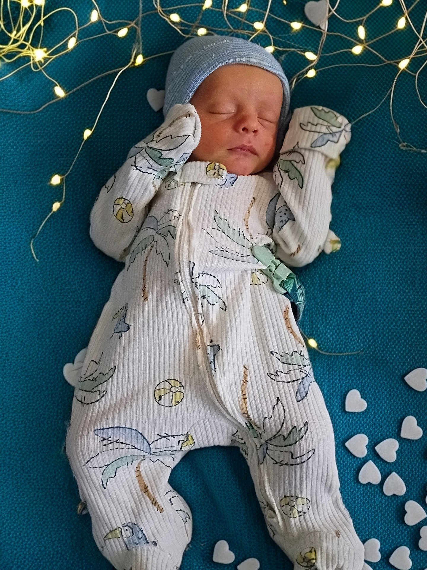 Leland Matthew is registered to the contest to win money with this photo: baby, newborn, infant, sleeping, hat, onesie, mittens, fairy_lights, heart_confetti, teal_background, cozy, portrait, cute, peaceful, pajamas, blanket, soft_lighting, closeup, nursery, decorative_hearts