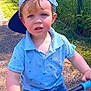 toddler, child, boy, blue_cap, blue_polo, balance_bike, outdoor, sunny_day, grip, path, fence, grass, curious_expression, shorts, blue_shoes, summer, daylight, nature, young_child, play