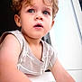 child, toddler, curly_hair, blue_eyes, indoor, window, curious, face, portrait, skin, young, sleeveless_shirt, light, expression, person, closeup, hair, eyelashes, mouth_open, arm