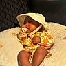 baby, infant, child, hat, yellow, floral_outfit, pillow, thumb_sucking, cute, indoors, soft_texture, relaxed, portrait, foot, cozy, sleepy, comfort, toddler, closeup, person