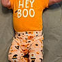 baby, bow, candy_corn, child, cute, face, footwear, ghost, halloween_theme, hands, happy, headband, infant, lying_down, orange_clothing, pants, pumpkin, smiling, sneakers, soft_surface