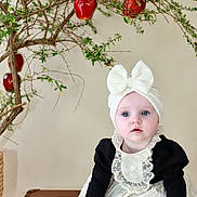 Savannah is registered to the contest to win money with this photo: baby, infant, child, dress, headband, bow, blue_eyes, suitcase, tree_branch, red_fruit, indoor, portrait, curious_expression, vintage_style, decor, soft_lighting, hands, feet, clothing, cute
