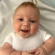 Alfie is registered to the contest to win money with this photo: baby, blanket, child, chubby_arms, closeup, cute, face, hands, happy, head, indoors, infant, joyful, lying_down, person, portrait, skin, smiling, soft, white_onesie