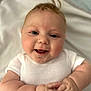 baby, blanket, child, chubby_arms, closeup, cute, face, hands, happy, head, indoors, infant, joyful, lying_down, person, portrait, skin, smiling, soft, white_onesie