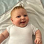 adorable, baby, blanket, child, chubby, closeup, cute, cute_expression, face, happy, indoor, infant, lying_down, portrait, skin, small_hands, smile, soft, white_onesie, young