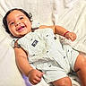 baby, child, infant, smiling, happy, portrait, lying_down, blanket, bed, indoor, romper, striped_clothing, fashion, dark_hair, brown_eyes, hands, arms, legs, closeup, cute