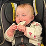 baby, child, car_seat, cracker, infant, safety_harness, onesie, floral_pattern, blue_eyes, cheeks, hand, legs, toy, padded_seat, warning_label, curious, indoor, cute, happy, gnawing