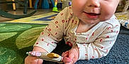 Valkyrie is registered to the contest to win money with this photo: baby, child, toy, carpet, indoor, blue_eyes, clothing, hand, face, smiling, floor, furniture, playroom, person, crawling, infant, home, cute, curious, light