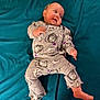 baby, infant, pajamas, sleepwear, lying_down, blanket, blue_background, cute, smiling, face, foot, hand, child, patterned_clothing, indoors, soft_fabric, person, cozy, relaxed, small_toddler