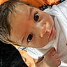 baby, infant, face, eyes, skin, hand, white_shirt, blanket, orange, pattern, closeup, portrait, cute, young_child, lying_down, human, expression, indoors, soft_texture, curious