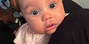 Kensie joined the competition — help win amazing prizes! baby, infant, face, eyes, polka_dot, clothing, indoor, furniture, television, wooden_clock, curious, skin, hand, arm, person, portrait, cute, closeup, sitting, expression