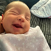 Kensie is registered to the contest to win money with this photo: baby, newborn, smiling, blanket, pink, heart_pattern, face, closeup, couch, indoor, resting, soft_texture, comfort, child, infant, happy, wrapped, cozy, portrait, relaxation