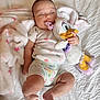 Kensie is registered to the contest to win money with this photo: baby, infant, sleepy, plush_toy, duck, blanket, white, pink, clothing, onesie, cuddling, cute, soft, bed, lying_down, peaceful, child, toy, comfort, resting