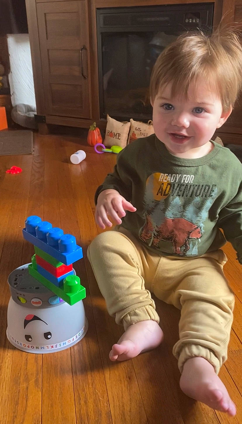 Wyatt is registered to the contest to win money with this photo: baby, baby_toddler_clothing, cabinetry, cheek, chest_of_drawers, child, cupboard, door, floor, flooring, fun, hardwood, person, refrigerator, sitting, sleeve, smile, t_shirt, toddler, toy