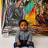 baby, child, infant, sitting, barefoot, checkered_shirt, jeans, curly_hair, portrait, indoor, mural, artwork, painting, colorful, birds, expression, face, cute, young, person