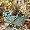 cat, tabby_cat, kitten, animal, pet, fur, whiskers, eyes, sitting, carriage, baby_carriage, vintage, turquoise, garden, flowers, cottage, outdoor, stone_path, rose, sunlight