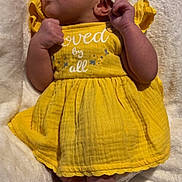Xureila is registered to the contest to win money with this photo: baby, infant, yellow_dress, headband, lying_down, soft_blanket, curious, toes, clothing, cute, small_hands, portrait, indoors, child, newborn, skin, face, expression, person, adorable