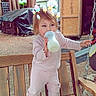 toddler, child, bottle, drinking, bench, outdoor, trees, shed, wood, boots, clothing, playful, filter, popsicle, digital_overlay, nature, daylight, person, standing, casual